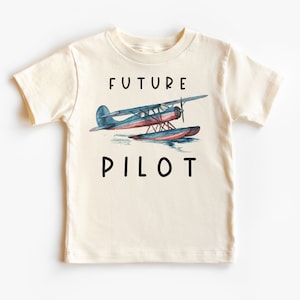 May include: A cream colored t-shirt with a blue and red seaplane graphic and the text "FUTURE PILOT" in black.
