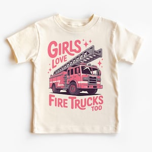 K&ouml;nnte beinhalten: Cremefarbenes T-Shirt mit einer rosa Feuerwehrauto-Grafik und dem Text "GIRLS LOVE FIRE TRUCKS TOO" in Rosa. Das Design enth&auml;lt Sterne, ideal f&uuml;r kleine Kinder.
