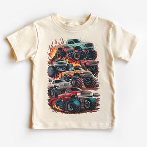 May include: A white t-shirt with a graphic of a stack of monster trucks with flames. The trucks are red, blue, yellow, and white.