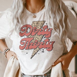 May include: A white t-shirt with a red and black graphic that says "Dirty Thirty" with a leopard print lightning bolt.