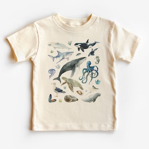 May include: A white t-shirt with a colorful watercolor illustration of various sea creatures, including a whale, shark, octopus, sea turtle, and seagull.