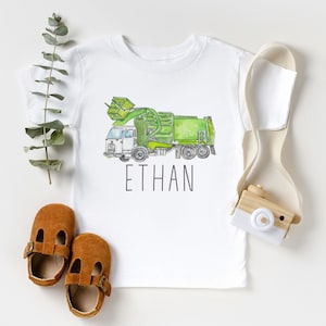 May include: White t-shirt with a green and white watercolor illustration of a garbage truck. The text "ETHAN" is printed below the truck.