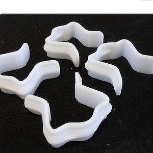 Puede incluir: Cinco clips de cortina de plástico blanco, cada uno con un diseño ondulado, están dispuestos en forma de estrella.