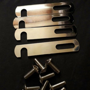 May include: A set of silver-colored metal brackets with elongated slots and curved ends, paired with a collection of silver screws. The hardware is arranged against a dark background, suggesting a product for construction or repair.