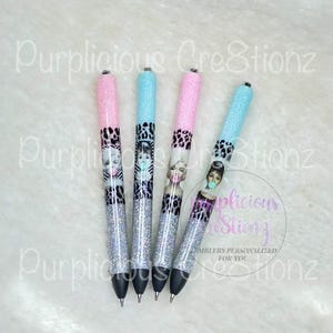 May include: Four glitter pens with pink, blue, and silver accents. Each pen features a different celebrity image and a leopard print design. The text "Purplicious Creations" is visible in the background.