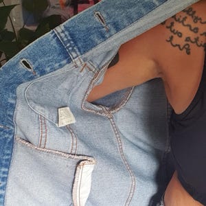 May include: A light blue denim jacket with a classic design. The jacket features a button-up front, pockets, and a light-wash denim fabric. The interior lining is visible, showing the stitching and construction details.