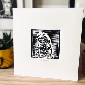 Peut inclure: Carte carr&eacute;e blanche avec une gravure sur linol&eacute;um en noir et blanc d'un chien Cockapoo. L'impression est encadr&eacute;e dans un cadre noir. Le mot "Cockapoo" est sous l'image, avec "2/10" et "SB" &eacute;galement pr&eacute;sents.