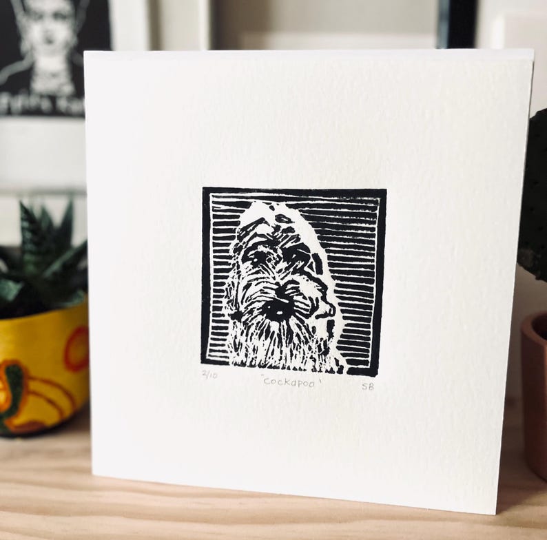Peut inclure: Carte carr&eacute;e blanche avec une gravure sur linol&eacute;um en noir et blanc d'un chien Cockapoo. L'impression est encadr&eacute;e dans un cadre noir. Le mot "Cockapoo" est sous l'image, avec "2/10" et "SB" &eacute;galement pr&eacute;sents.