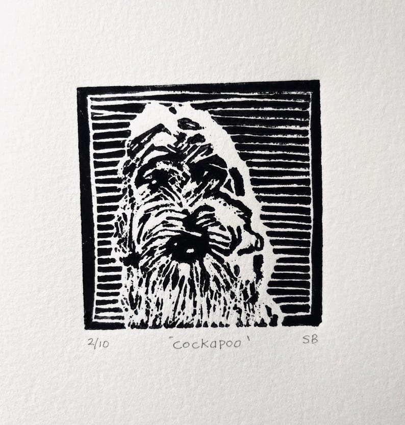 Peut inclure: Gravure en linogravure en noir et blanc d'un visage de chien Cockapoo, encadr&eacute; dans un rectangle noir. Le pelage du chien est d&eacute;taill&eacute; avec des lignes textur&eacute;es. L'impression est num&eacute;rot&eacute;e 2/10, avec le mot 'cockapoo' et les initiales de l'artiste.