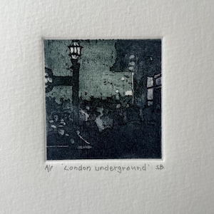 May include: A small, framed print depicting a nighttime scene of the London Underground. The artwork, in shades of gray and teal, features a lamppost, buildings, and the text "London underground".