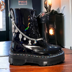 May include: Black leather boots with a chunky platform sole and a silver chain with charms, including owls and a heart, attached to the ankle. The boots have a rainbow colored stitching detail around the sole.