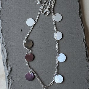 May include: A silver-toned chain necklace featuring multiple small, flat, circular charms in alternating metallic silver and dark brown finishes. The necklace includes a lobster claw clasp and a short extender chain for adjustable length.