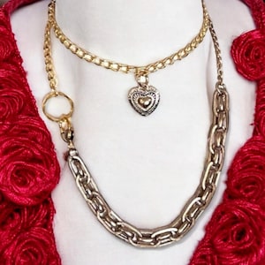 May include: Two gold chains with a heart pendant. The top chain is a delicate curb chain and the bottom chain is a thicker, chunky chain.