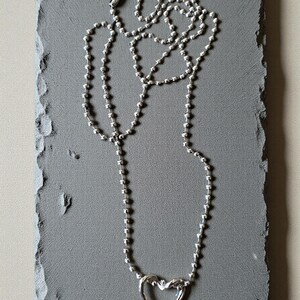 May include: A silver-toned ball chain necklace featuring a polished heart-shaped pendant. The necklace is constructed from small, uniform spherical beads linked together, ending in a secure barrel-style clasp at the top of the chain.