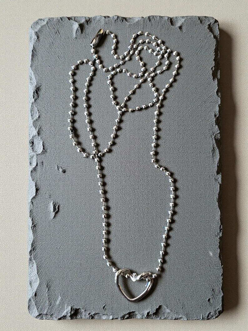 May include: A silver-toned ball chain necklace featuring a polished heart-shaped pendant. The necklace is constructed from small, uniform spherical beads linked together, ending in a secure barrel-style clasp at the top of the chain.
