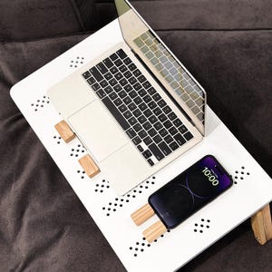 May include: A white laptop desk with a laptop and a smartphone. The desk has a perforated surface and wooden supports. The smartphone displays the time as 10:00. The laptop is silver.