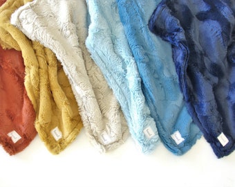 Puede incluir: Cinco mantas de felpa en diferentes colores, incluyendo óxido, amarillo mostaza, beige, azul claro y azul marino. Cada manta tiene una pequeña etiqueta blanca con la palabra "boo" impresa en ella.