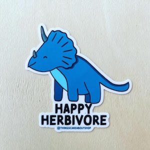 May include: A blue triceratops sticker with a light blue underbelly and dark blue horns. The text below the dinosaur reads HAPPY HERBIVORE in black capital letters, followed by the smaller text @THINGSICAREABOUTSHOP in blue.