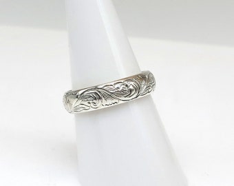 Puede incluir: Un anillo de plata con un intrincado diseño floral. El anillo se muestra en un soporte cónico blanco.