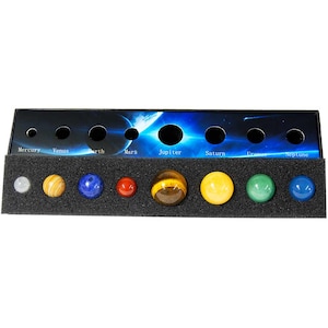 May include: A solar system model featuring nine colorful gemstone spheres representing the planets, each labeled with its name. The planets are arranged in a row on a black foam base, with a cosmic background.
