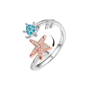 Puede incluir: Anillo plateado con una tortuga turquesa y una estrella de mar en oro rosa, ambas con detalles de cristal. La estrella de mar gira. Un cristal cuadrado está engastado en la banda. Tema náutico.