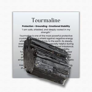May include: A rough, black tourmaline crystal is displayed in front of a white card. The card has the word "Tourmaline" at the top, with text below describing its properties: Protection, Grounding, and Emotional Stability.