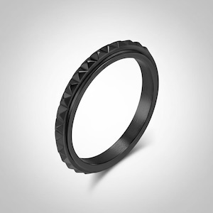 Può includere: Un anello nero con un design geometrico strutturato sul bordo esterno. L'anello è realizzato in un materiale scuro e opaco e ha una fascia interna liscia. L'anello è mostrato su uno sfondo bianco.