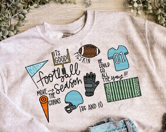 May include: A gray sweatshirt with a football theme design. The design includes the words "It's good!" "Football Season" "Move the Chains" "Pigskin" "He could go all the way!" "1st and 10" and "Touchdown". The design also includes a football, a football helmet, a football field, a football glove, and a football jersey.
