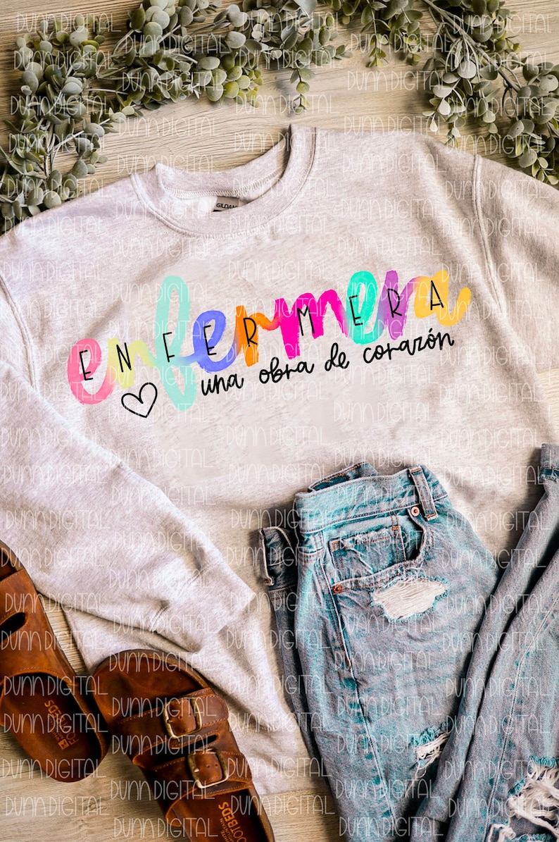 May include: A gray sweatshirt with the text "Enfermera una obra de coraz&oacute;n" in rainbow colors. The text is in a handwritten style with a heart symbol.