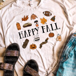 以下が含まれることがあります： 秋をテーマにしたアイコンと「HAPPY FALL」というテキストが描かれた白いTシャツ。アイコンには、かぼちゃ、コーヒーカップ、マフラー、フットボール、パイ、葉っぱ、セーター、丸太、帽子などが含まれています。