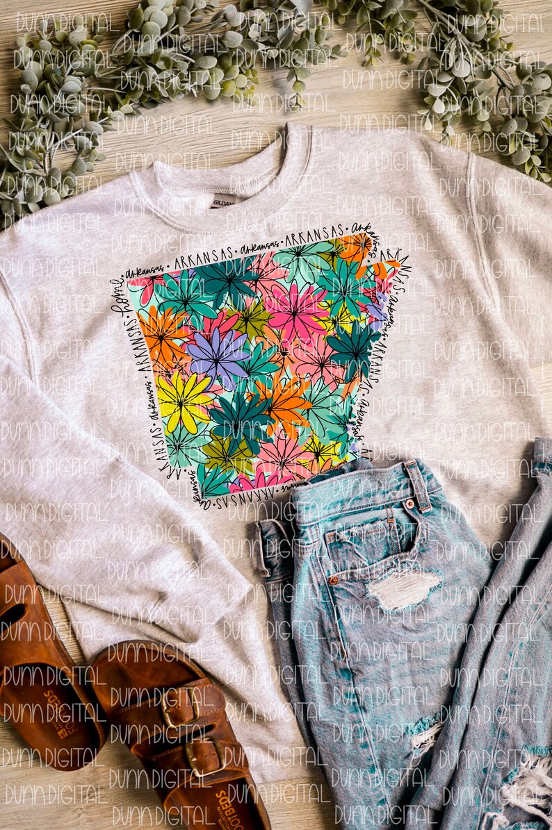 May include: A gray sweatshirt with a floral design of the state of Arkansas. The design is outlined in black and filled with colorful flowers. The words "Arkansas - Arkansas - Arkansas" are written around the outline of the state.