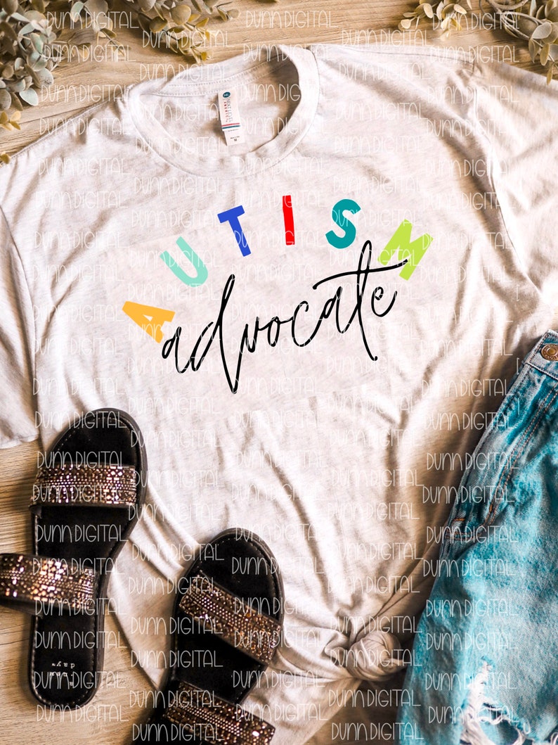 May include: A white t-shirt with the words "AUTISM advocate" in colorful letters. The letters are in different colors, including blue, red, green, yellow, and orange. The words are written in a cursive font.
