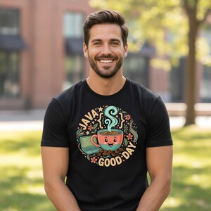 Peut inclure: T-shirt noir avec un motif color&eacute; d'une tasse de caf&eacute; souriante avec de la vapeur, un ordinateur portable et des grains de caf&eacute;. Le texte "JAVA GOOD DAY" est int&eacute;gr&eacute; au design. Le t-shirt est port&eacute; par une personne.