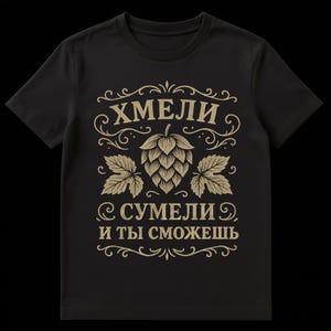 Pode incluir: T-shirt preta com um gráfico dourado com um cone de lúpulo e folhas, com texto decorativo. O texto diz "ХМЕЛИ" acima do cone de lúpulo e "СУМЕЛИ И ТЫ СМОЖЕШЬ" abaixo.