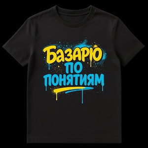 Puede incluir: Camiseta negra con el texto "Базарю по понятиям" en letras amarillas y azules estilo grafiti. El diseño presenta goteos de pintura y un efecto de pintura en aerosol, creando una estética audaz y urbana.