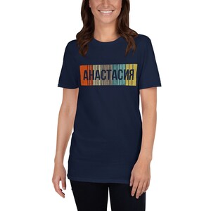 May include: A navy blue t-shirt with a retro-style graphic of the word "Анастасия" in a colorful striped design.