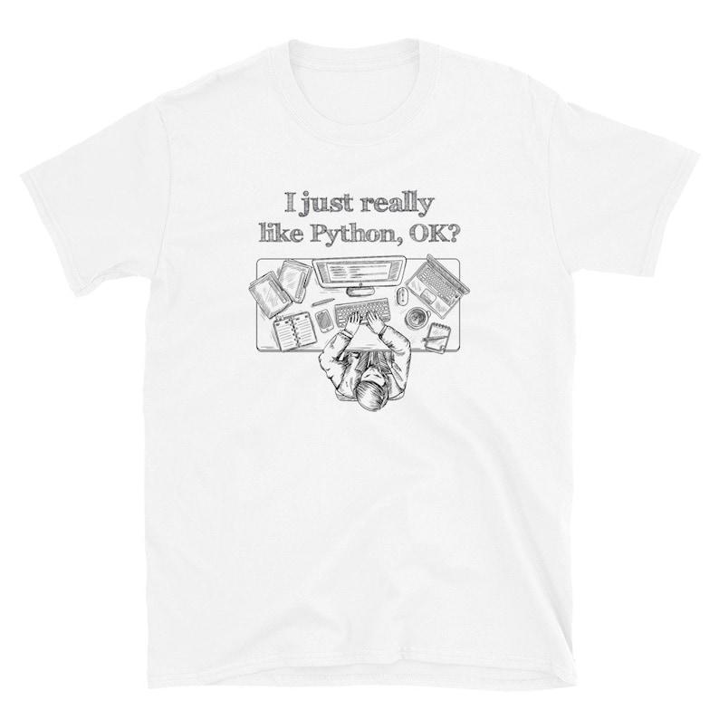 May include: White t-shirt with a black and white graphic of a person at a desk with a computer, books, and a laptop. The text "I just really like Python, OK?" is above the desk. The shirt is made of a soft material.