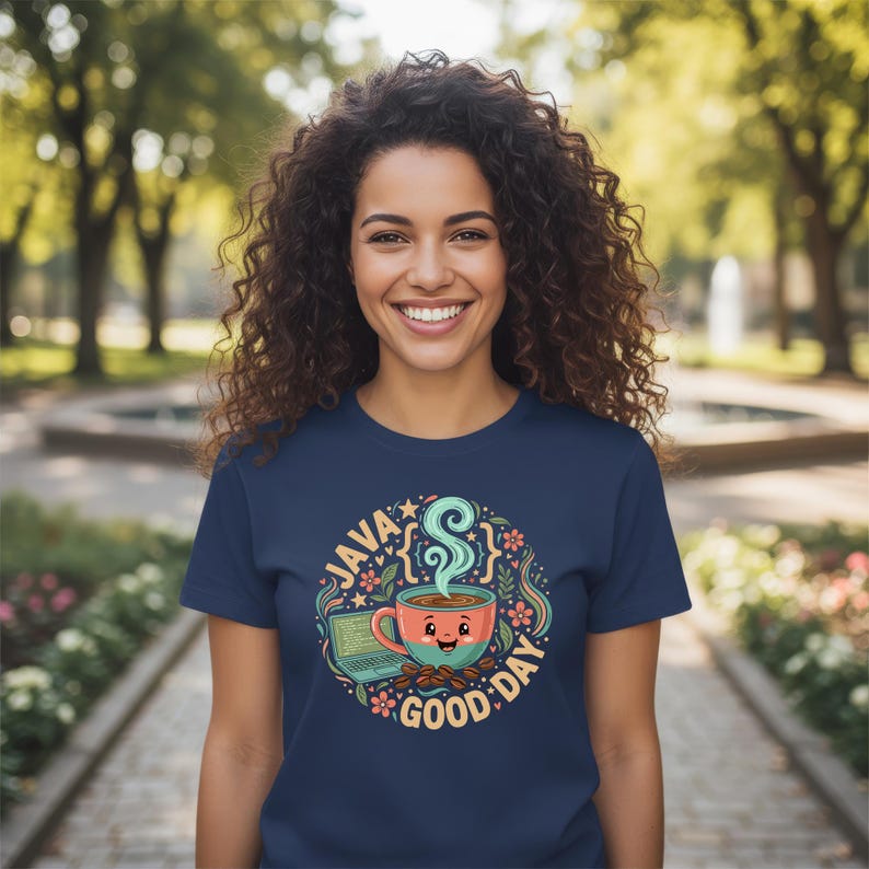 Peut inclure: T-shirt bleu marine avec un motif color&eacute; repr&eacute;sentant une tasse de caf&eacute;, un ordinateur portable et l'inscription "JAVA GOOD DAY". Le design comprend des &eacute;l&eacute;ments floraux et &eacute;toil&eacute;s. La personne porte le t-shirt et sourit.