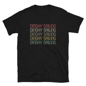 May include: Black t-shirt with the text "DINGHY SAILING" repeated in a retro style. The text is in shades of red, orange, yellow, and green. The shirt is made of a soft material.