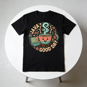 Peut inclure: T-shirt noir avec un motif color&eacute; repr&eacute;sentant une tasse de caf&eacute; souriante avec de la vapeur, entour&eacute;e d'&eacute;l&eacute;ments floraux et de grains de caf&eacute;. Le texte "JAVA GOOD DAY" est dispos&eacute; en cercle autour de la tasse. Un ordinateur portable est &eacute;galement inclus.