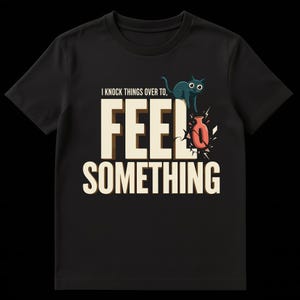 Könnte beinhalten: Schwarzes T-Shirt mit dem Text "I knock things over to, FEEL SOMETHING". Eine teal-farbene Katze sitzt über einer zerbrochenen Vase. Der Text ist fett und cremefarben.