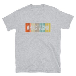 May include: A gray t-shirt with a vintage-style graphic of the word "Anastasia" in white letters with a rainbow stripe background.