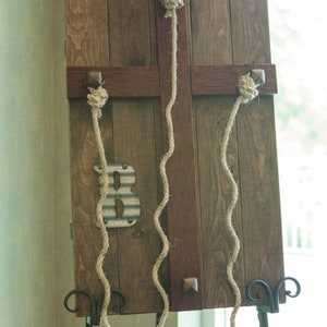 May include: A rustic wooden sign with a metal letter "B" and three pieces of twine hanging from the top. The sign is on a black metal easel.
