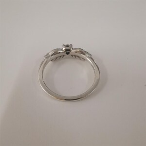 May include: A silver ring with a heart-shaped design and a small black stone in the center. The ring is decorated with intricate details on the sides.