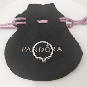 May include: A silver ring with a clear stone in the center and black stones on the band. The ring is in a black velvet pouch with the word 'PANDORA' printed on it.