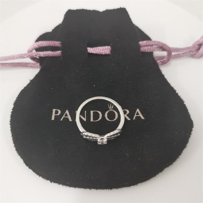 May include: A silver ring with a clear stone in the center and black stones on the band. The ring is in a black velvet pouch with the word 'PANDORA' printed on it.