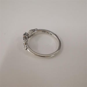 May include: A silver ring with a floral design and a small black stone. The ring is engraved with the text 'S 925 ALE 5G'.