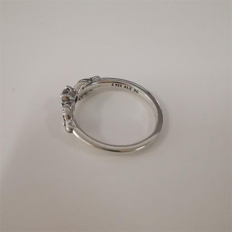 May include: A silver ring with a floral design and a small black stone. The ring is engraved with the text 'S 925 ALE 5G'.