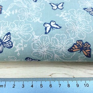 May include: A light blue fabric with a white floral pattern and colorful butterfly designs. The fabric is measured with a ruler in inches.