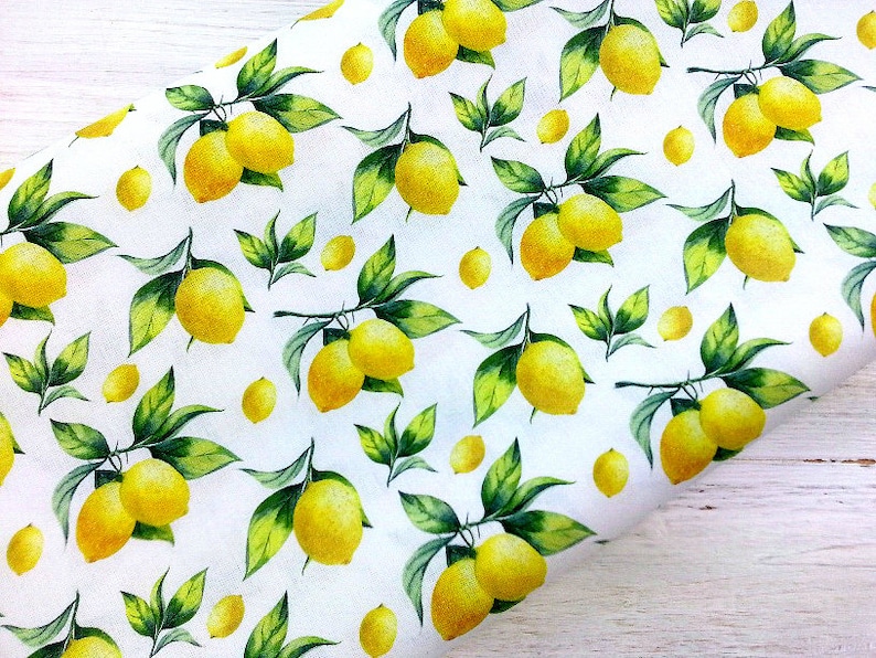 May include: White fabric with a repeating pattern of yellow lemons and green leaves. The lemons are arranged in clusters on branches.